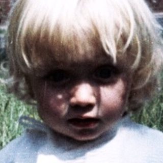 Young child standing outdoors in grassy area.