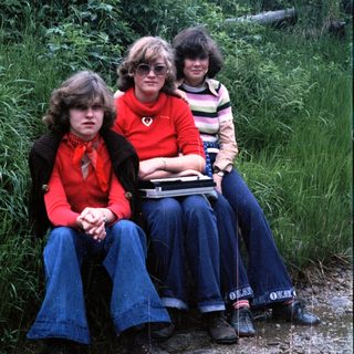 Three people sitting outdoors in 1970s-style clothing.