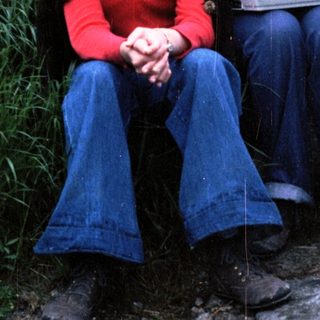 Three people sitting outdoors in 1970s-style clothing.