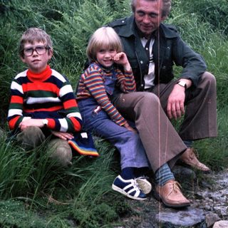 Family trio sitting outdoors on rocky path.