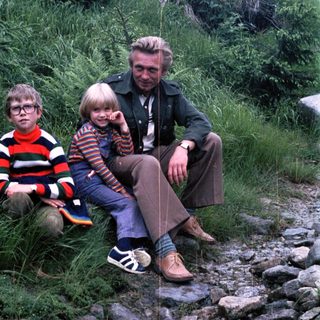 Family trio sitting outdoors on rocky path.
