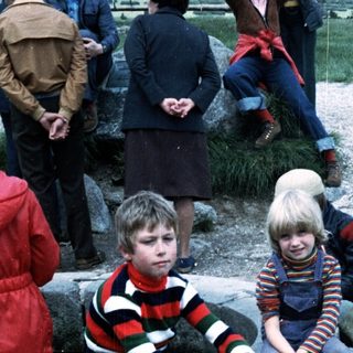 Two children sitting on rocks outdoors during an event.