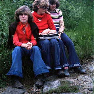 Three people sitting outdoors on rocks, holding a laptop.