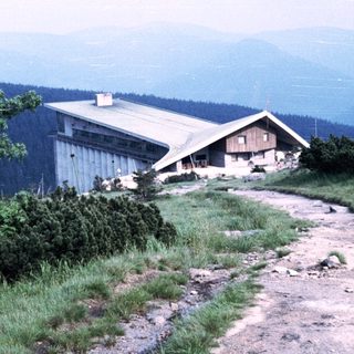 Mountain refuge building atop forested hillside.
