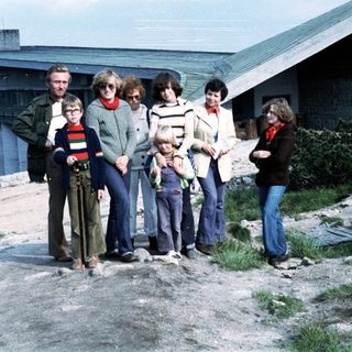 Family group posing outdoors near coastal buildings.