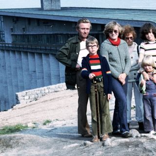 Family group posing outdoors near coastal buildings.