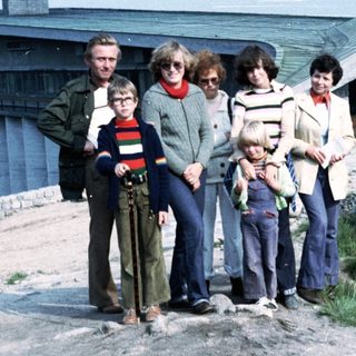 Family group posing outdoors near coastal buildings.