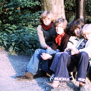Five people sitting outdoors in a wooded area.