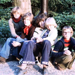 Five people sitting outdoors in a wooded area.