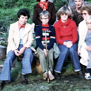 Group of eight people posing outdoors in forest setting.