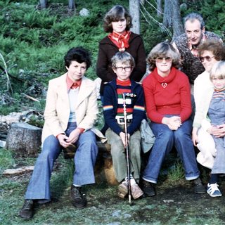 Group of eight people posing outdoors in forest setting.