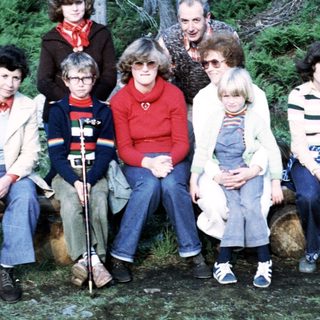 Group of eight people posing outdoors in forest setting.