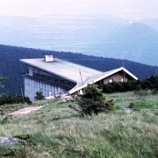 Mountain refuge or chalet on elevated grassy terrain.
