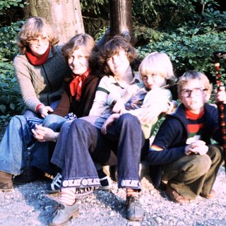 Five people posing together outdoors in a wooded area.
