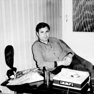 Man seated with vintage reel-to-reel recording equipment.