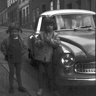 Two men posing by vintage car on city street.
