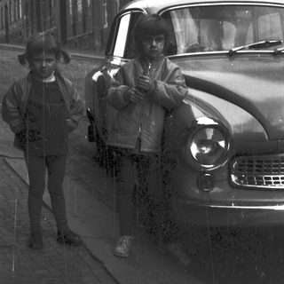 Two men posing by vintage car on city street.