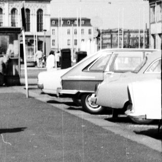 Woman in 1960s coat standing near bus station.