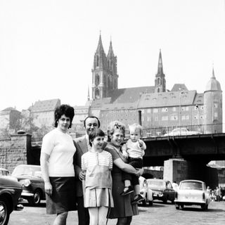 Family posing near historic cathedral with vintage cars.