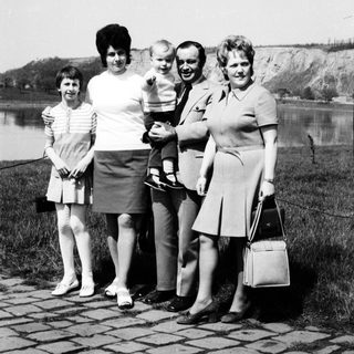 Family portrait by water with four adults and a baby.