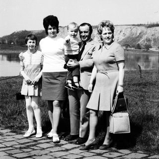 Family portrait by water with four adults and a baby.