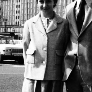 Two people posing together in formal attire, 1950s-60s urban setting.