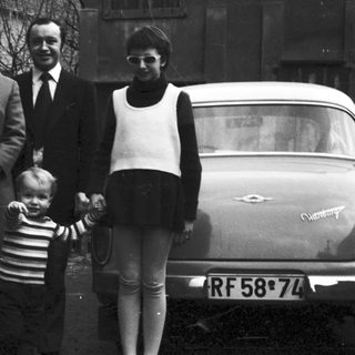 Family portrait with four adults and a child in front of a car, 1960s.