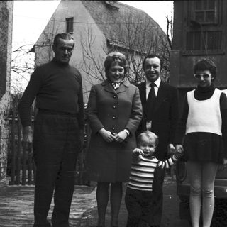 Family portrait with four adults and a child in front of a car, 1960s.