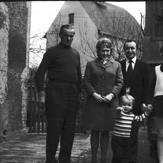 Family portrait with four adults and a child in front of a car, 1960s.