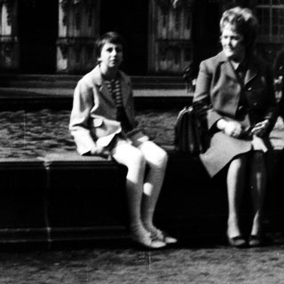 Three people sitting by a fountain in front of historic palace.
