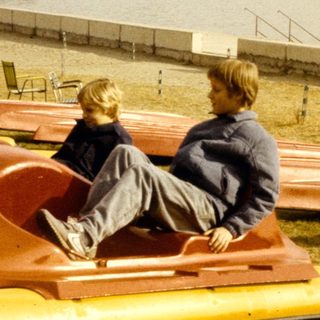 Two people sitting on pedal boats by a lake.