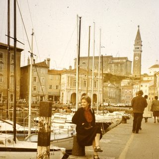 Vintage harbor scene with woman sitting near docked boats.