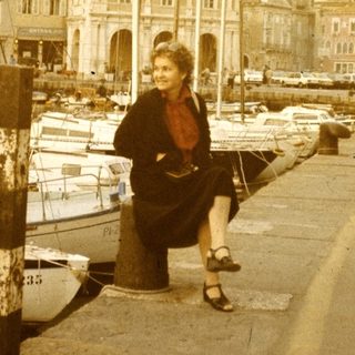 Vintage harbor scene with woman sitting near docked boats.