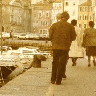 Vintage harbor scene with woman sitting near docked boats.