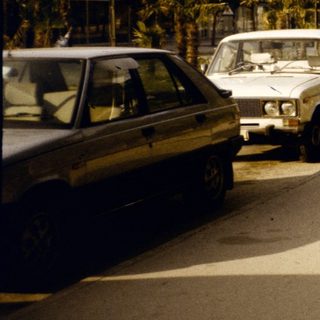 People walking on sidewalk near parked cars.