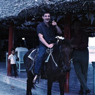 Man riding horse in outdoor area with thatched roof.