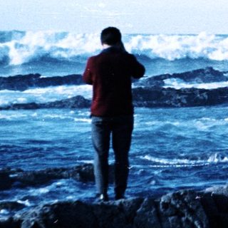 Person standing on rocks by crashing waves.