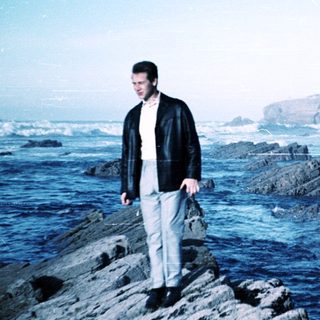 Man standing on rocks by ocean near lighthouse.