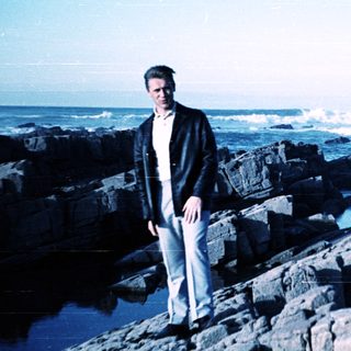 Man standing on rocky coastline near ocean waves.