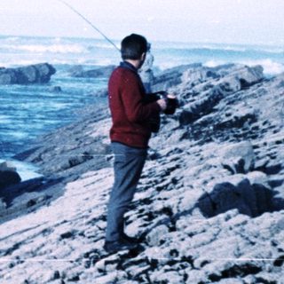 Person fishing near rocky coastline by ocean.
