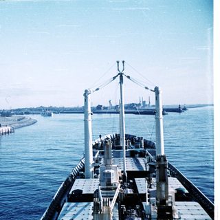 Maritime scene with ship, lighthouse, and harbor breakwater.