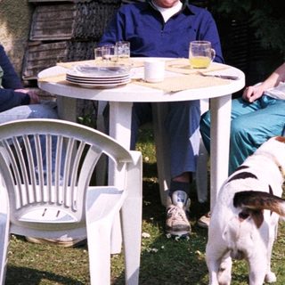Three men sitting outdoors with a dog, relaxing at a small table.