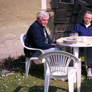 Three men sitting outdoors with a dog, relaxing at a small table.
