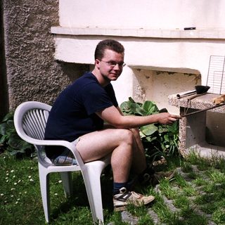 Man grilling meat outdoors near brick oven.