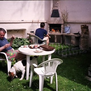 Two men, dog, and outdoor table with food.