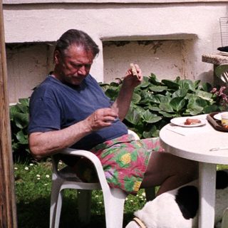 Two men, dog, and outdoor table with food.