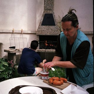 Woman preparing food by outdoor fireplace.
