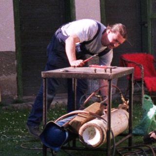 Man working on RV plumbing outside with dog nearby.
