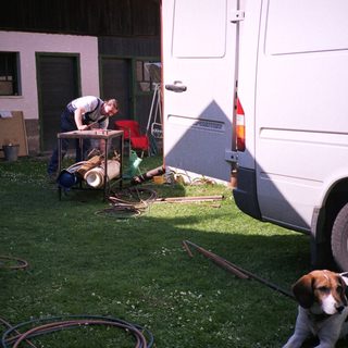 Man working on RV plumbing outside with dog nearby.
