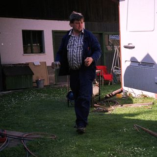 Man washing camper exterior with hose, dog nearby.